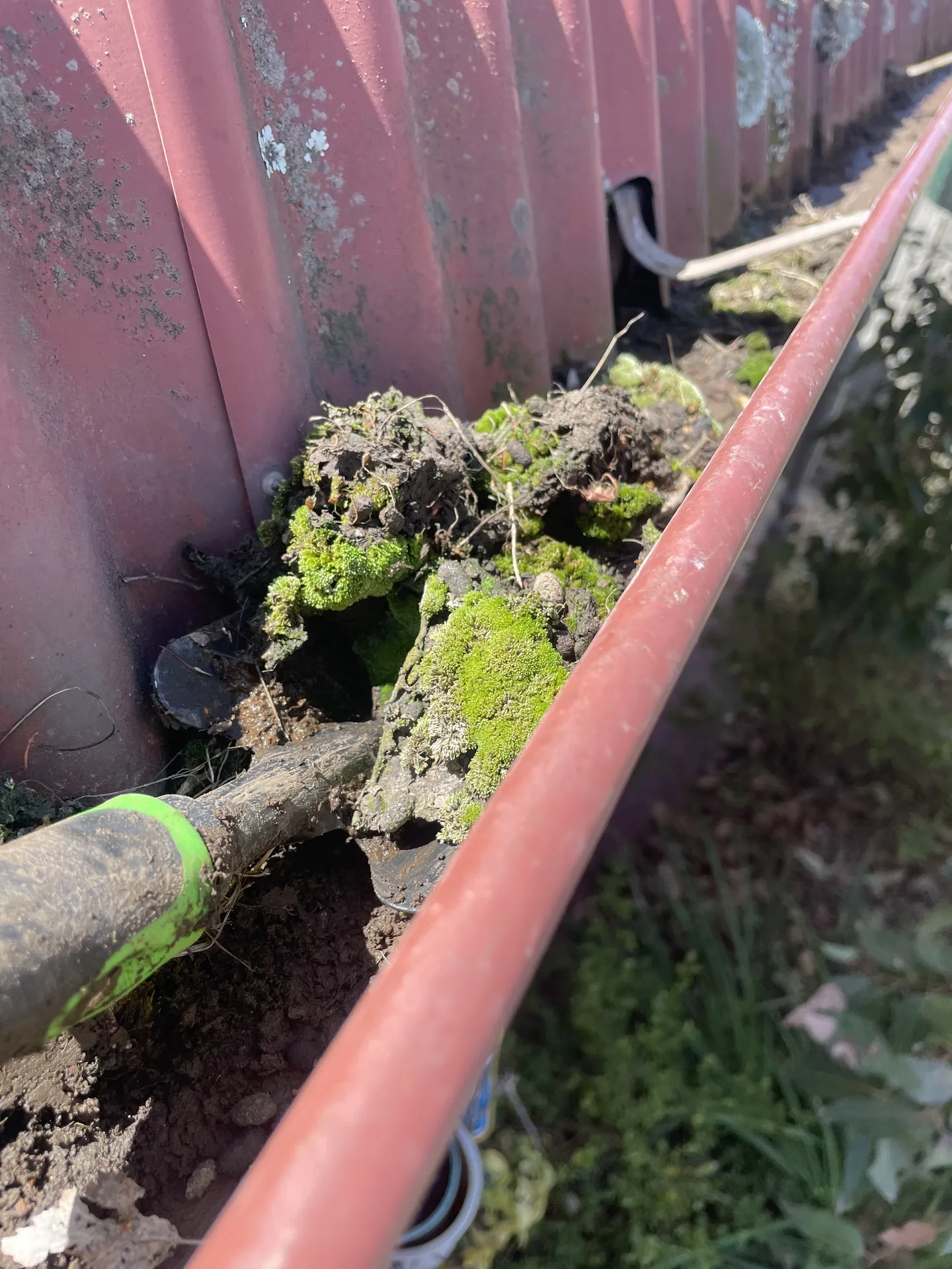 A shovel clearing dirt and moss sludge from a metal roof gutter